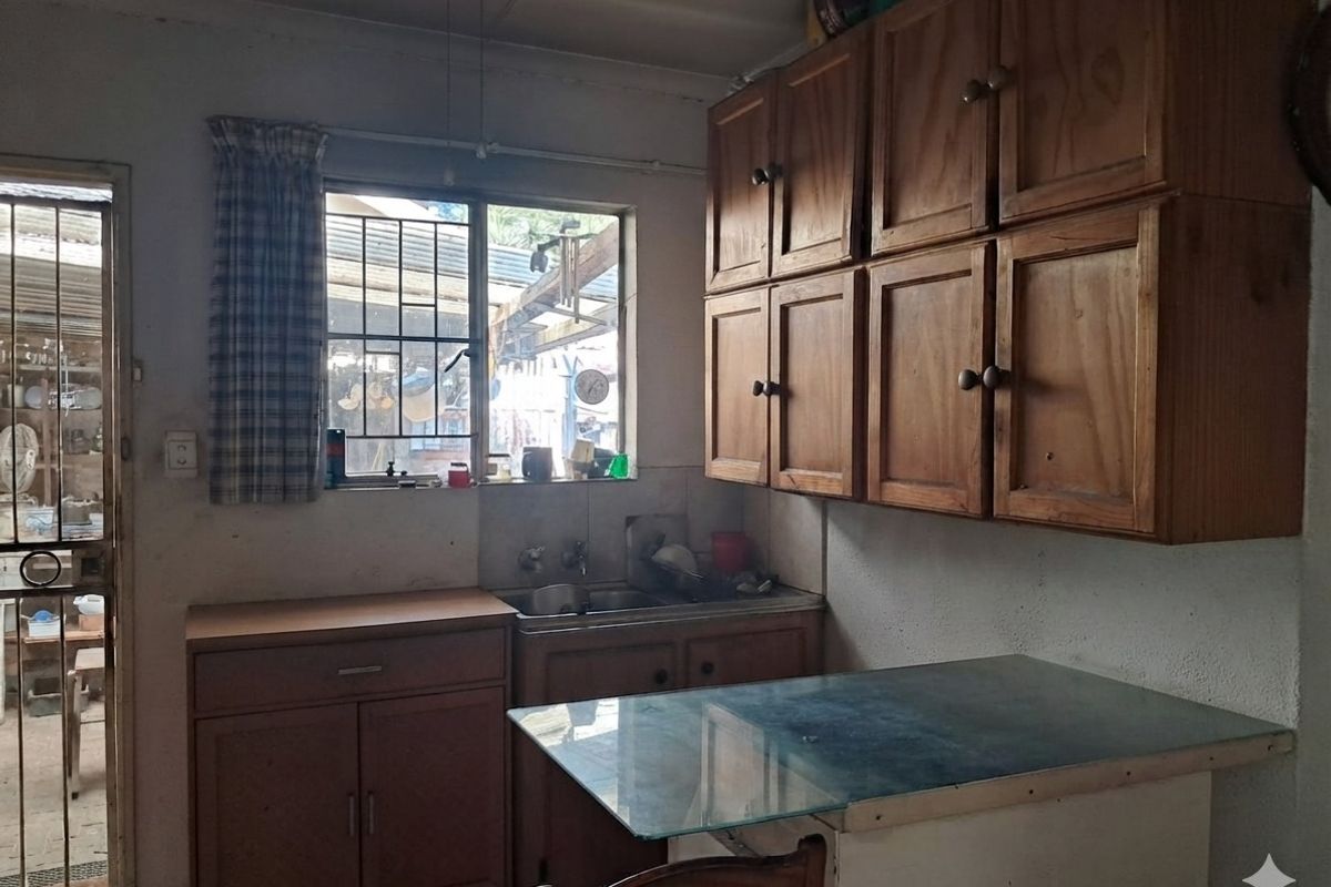 A dated kitchen featuring wooden cabinetry, a double basin sink, and direct access to an outdoor area through a security gate.