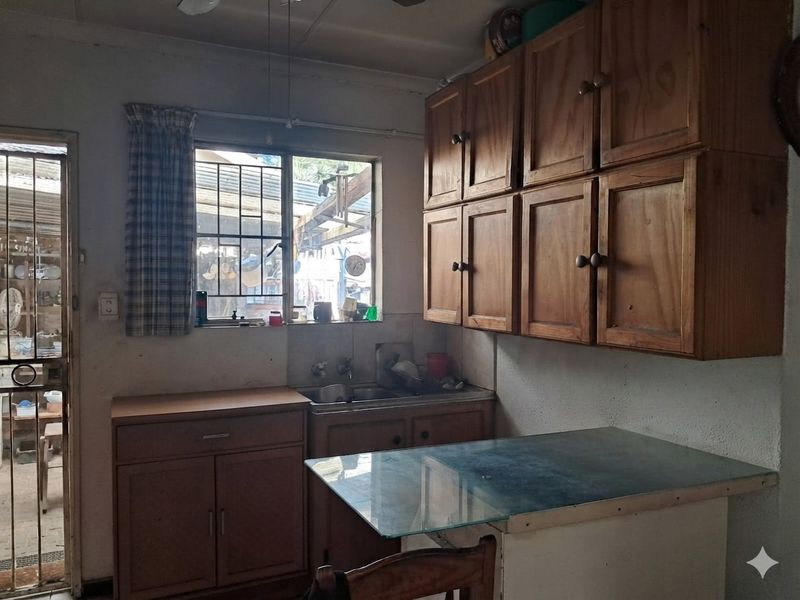 A dated kitchen featuring wooden cabinetry, a double basin sink, and direct access to an outdoor area through a security gate.