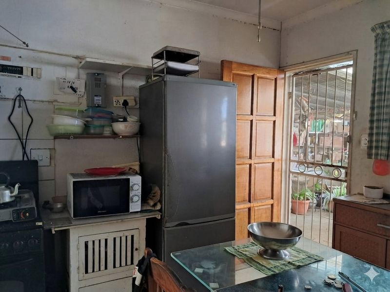 A dated kitchen area featuring a wooden door with a security gate, tiled splashbacks, and basic cabinetry, requiring cosmetic updates to modernize the space.