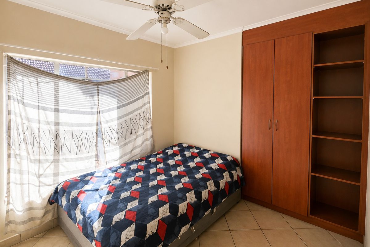 A bedroom featuring tiled flooring, a ceiling fan, and integrated wooden cabinetry including a built-in wardrobe and open shelving.