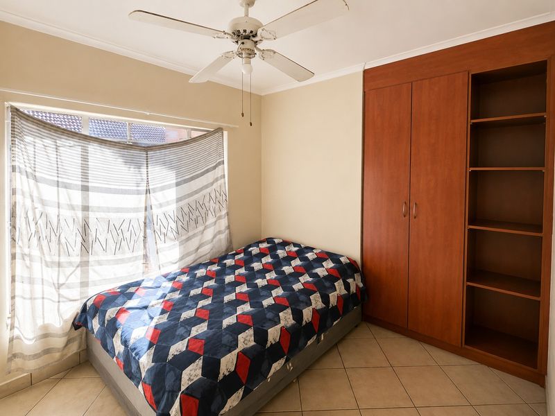A bedroom featuring tiled flooring, a ceiling fan, and integrated wooden cabinetry including a built-in wardrobe and open shelving.