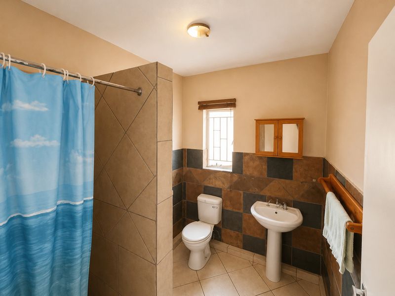 A functional bathroom featuring a pedestal basin, toilet, and a tiled shower area with a partition wall and security-barred window.