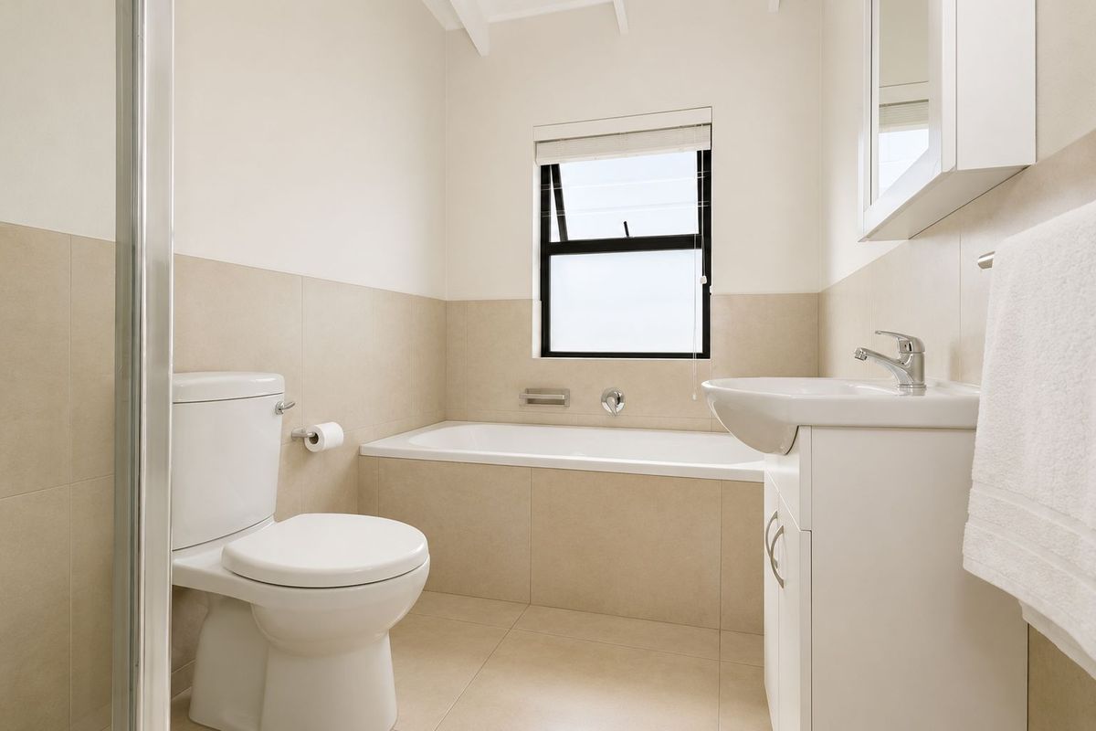 A clean, modern bathroom featuring a built-in bathtub, vanity cabinet with basin, toilet, and a separate shower enclosure with neutral wall and floor tiling.
