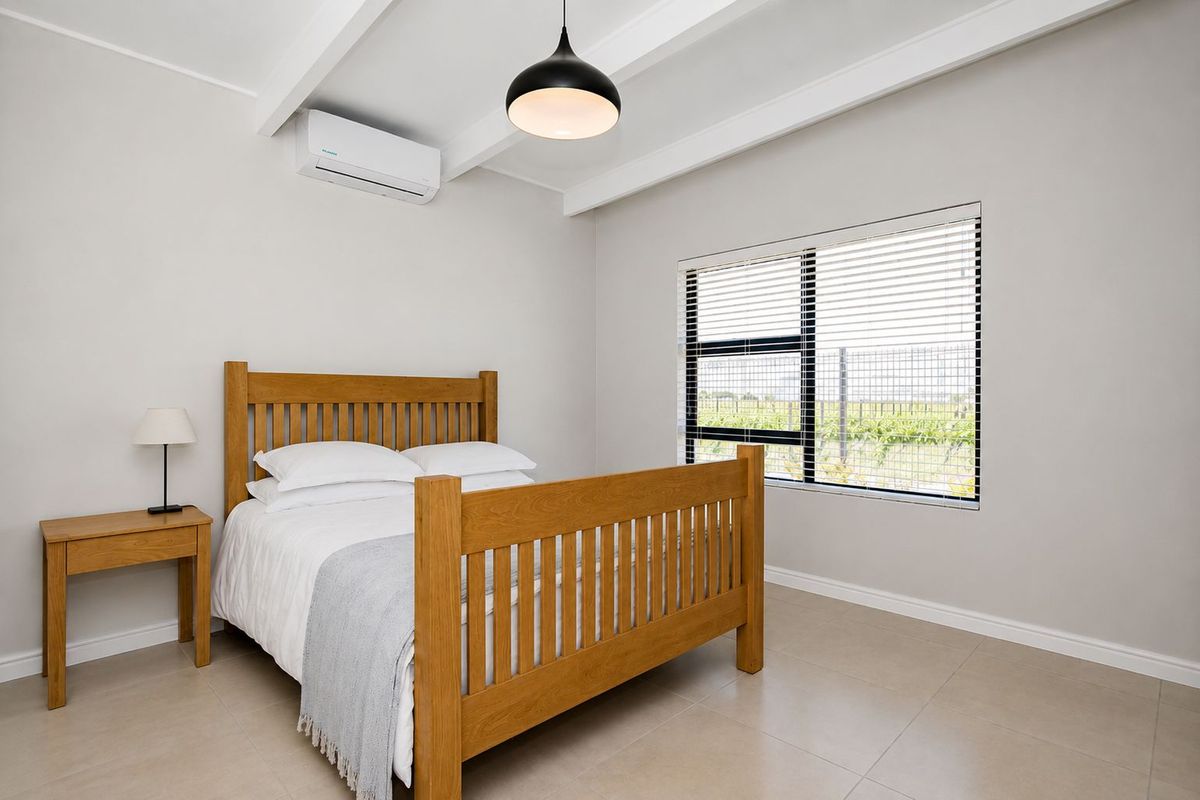 A bright and well-maintained bedroom featuring tiled flooring, exposed ceiling beams, and a split-system air conditioner.