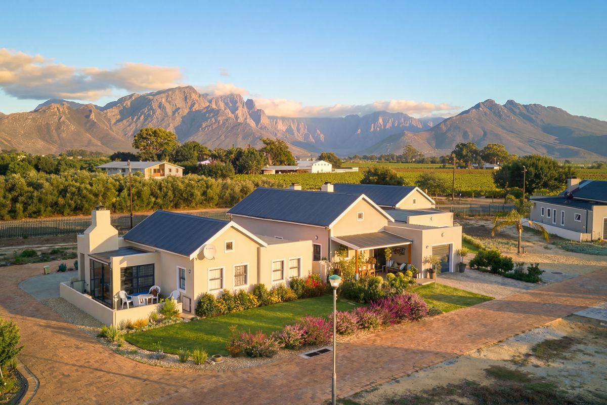 Aerial view of a well-maintained residential property featuring a metal roof, paved driveway, and landscaped garden with scenic mountain views.