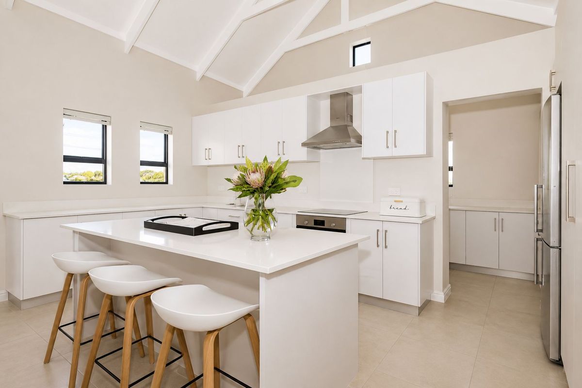 Modern kitchen featuring white cabinetry, stone countertops, a central island, and high vaulted ceilings, with an adjacent scullery area.