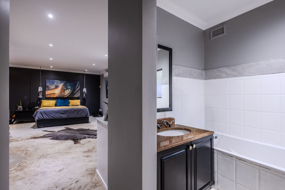 Open-plan bedroom featuring a connected ensuite bathroom with a built-in vanity, stone countertop, and bathtub, finished with modern dark wall accents.