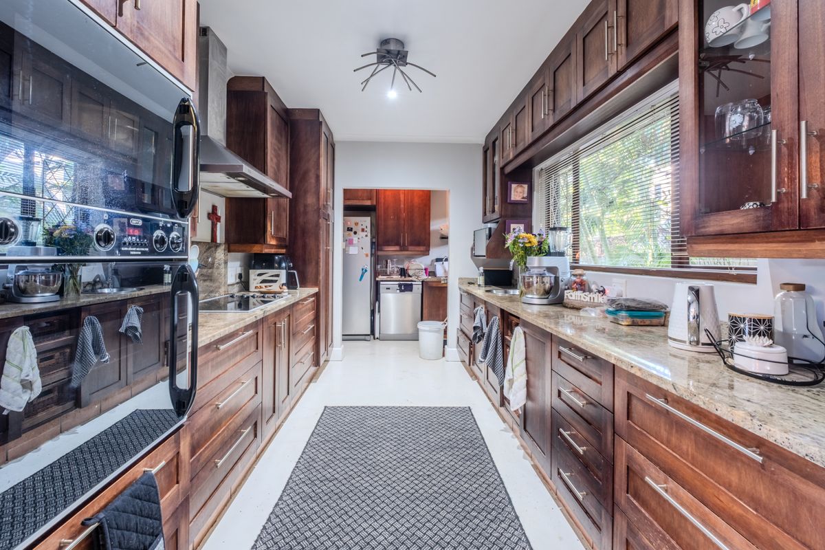 A well-appointed galley kitchen featuring rich wood cabinetry, granite countertops, integrated double wall ovens, and a dedicated scullery area visible through the doorway.