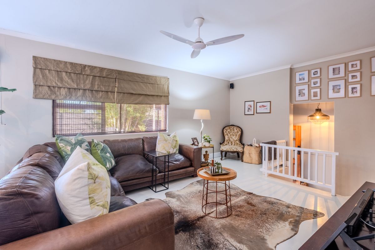A well-lit living room featuring painted timber flooring, a ceiling fan, and an open staircase with a white balustrade.