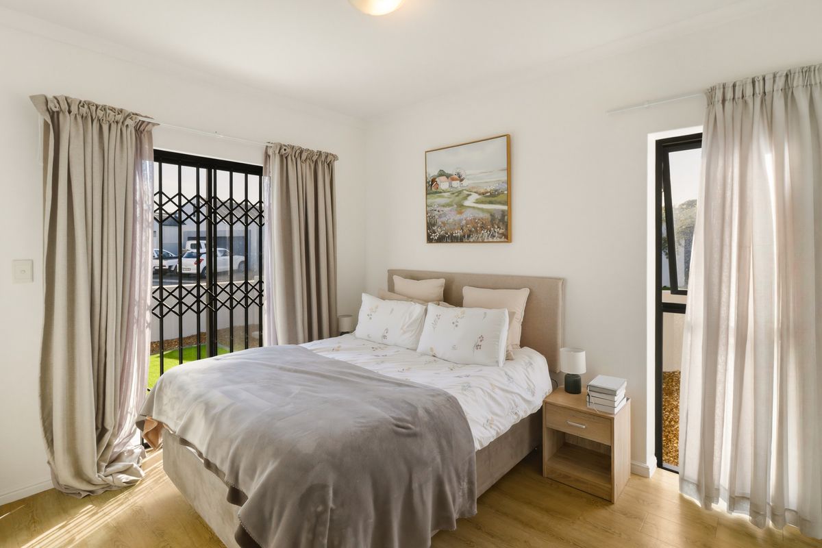 A bright bedroom featuring laminate flooring, a sliding door with security gate, and a casement window, offering natural light and direct outdoor access.