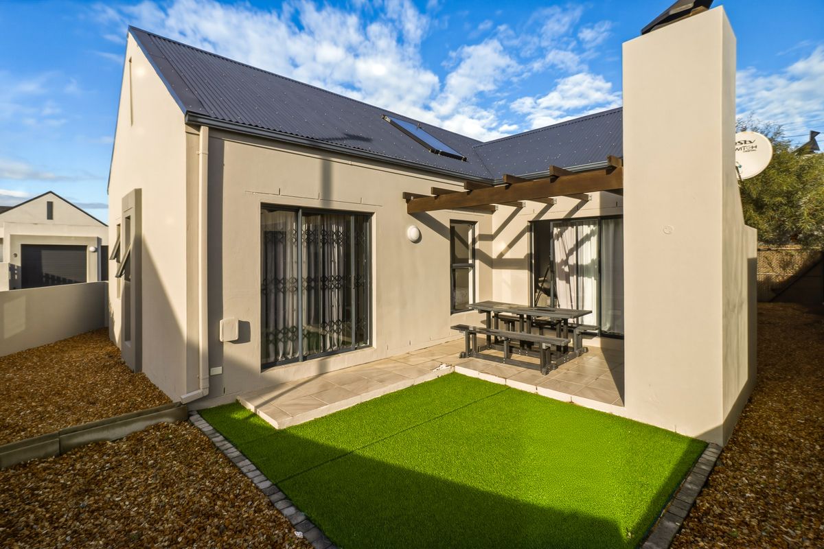 Rear exterior view featuring a paved patio with a timber pergola, artificial lawn, and modern sliding door access to the home.