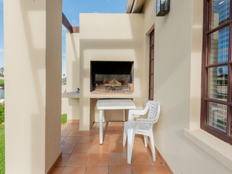 Covered patio area featuring a built-in braai, tiled flooring, and direct access to the garden and waterfront.