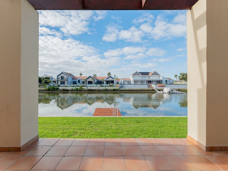 A covered patio featuring tiled flooring and timber pergola, offering direct views over the lawn toward the canal and private jetty.