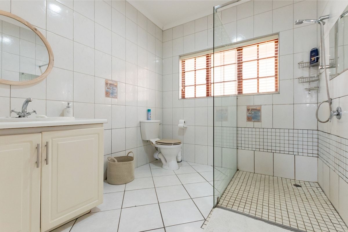 A functional bathroom featuring a vanity cabinet, a walk-in shower with a glass screen, and white tiled finishes throughout.