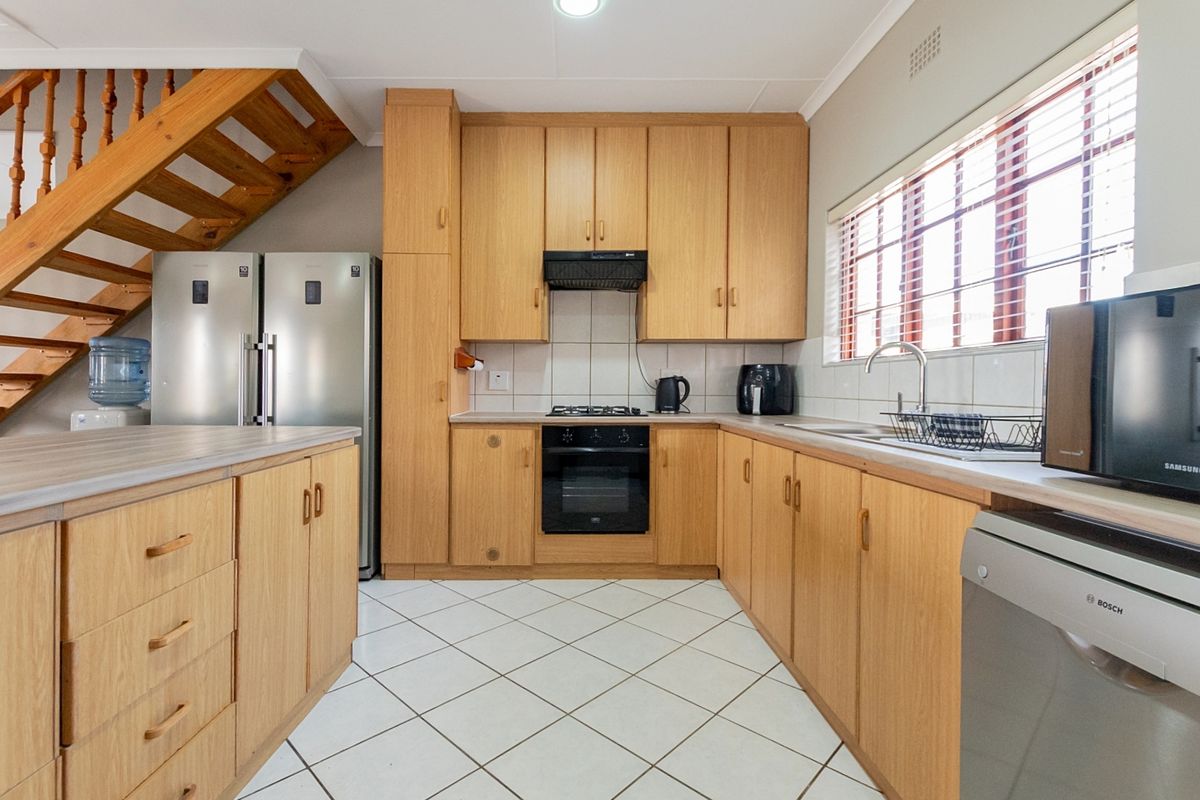Functional kitchen featuring light wood cabinetry, laminate countertops, built-in oven and hob, tiled flooring, and an adjacent wooden staircase.
