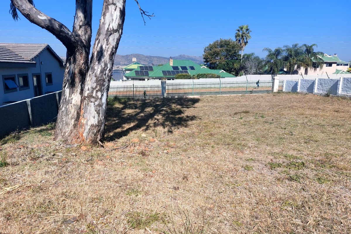 A vacant residential plot featuring a mature tree and perimeter fencing, offering a clear view of the surrounding neighborhood and distant hills.