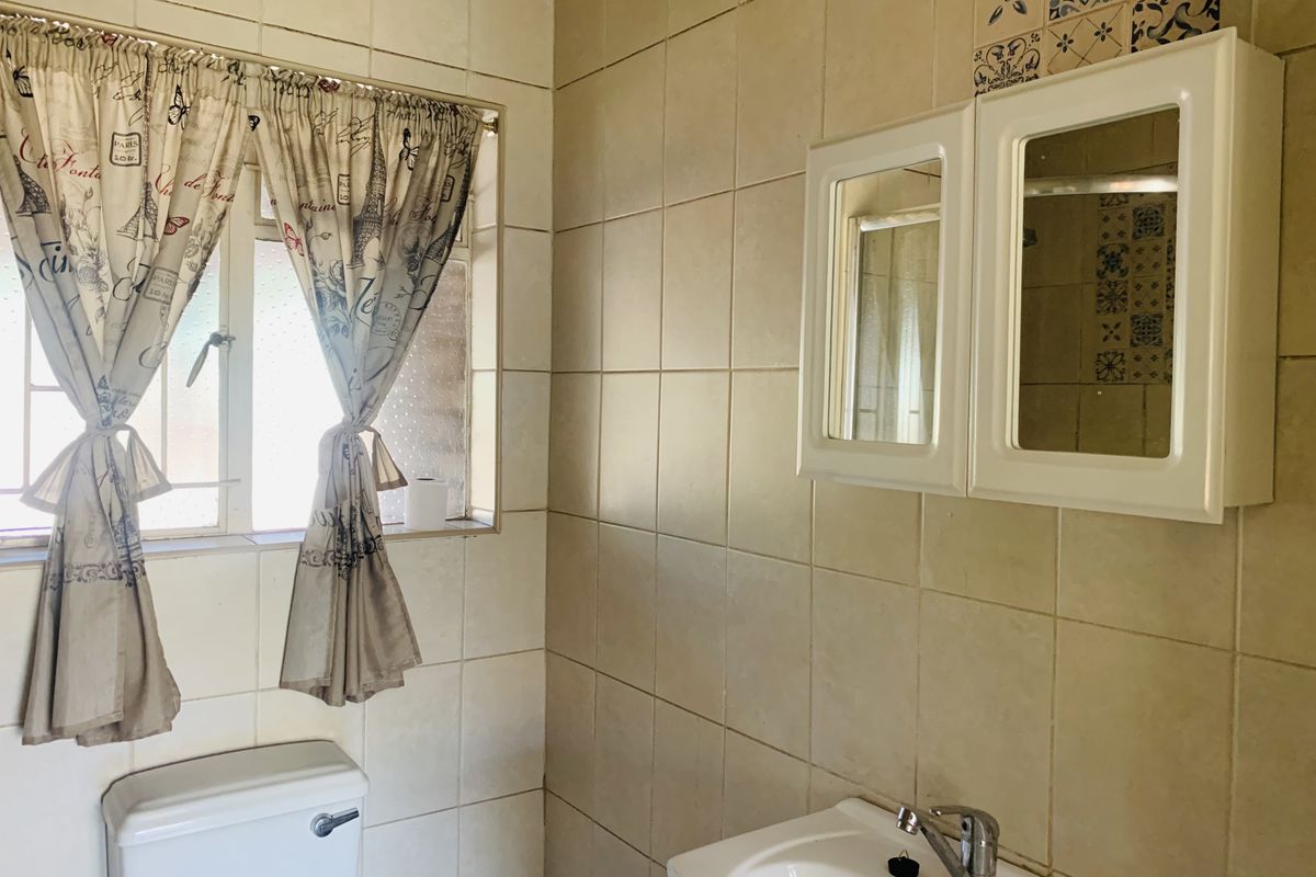 A functional bathroom featuring ceramic wall tiles, a wall-mounted vanity cabinet with mirrors, a washbasin with a chrome mixer tap, and a standard toilet.