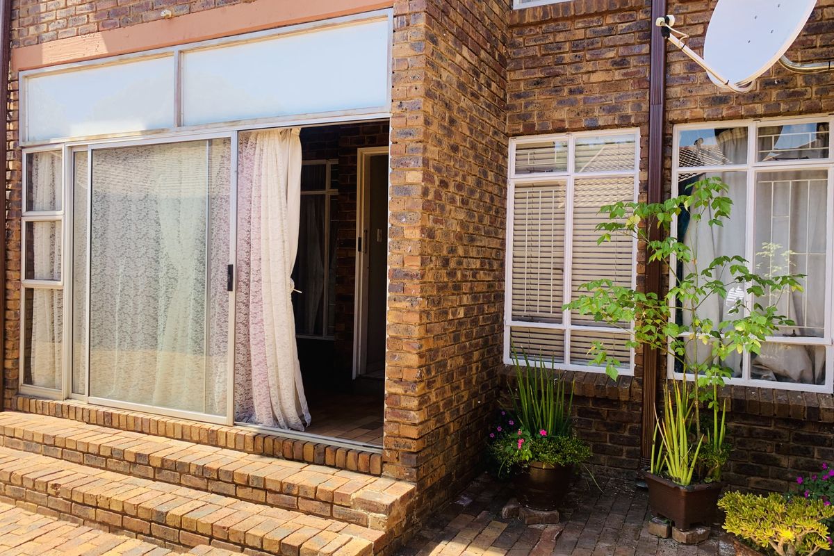 Rear exterior view of a face brick flat featuring a paved patio, brick steps, and sliding glass door access.