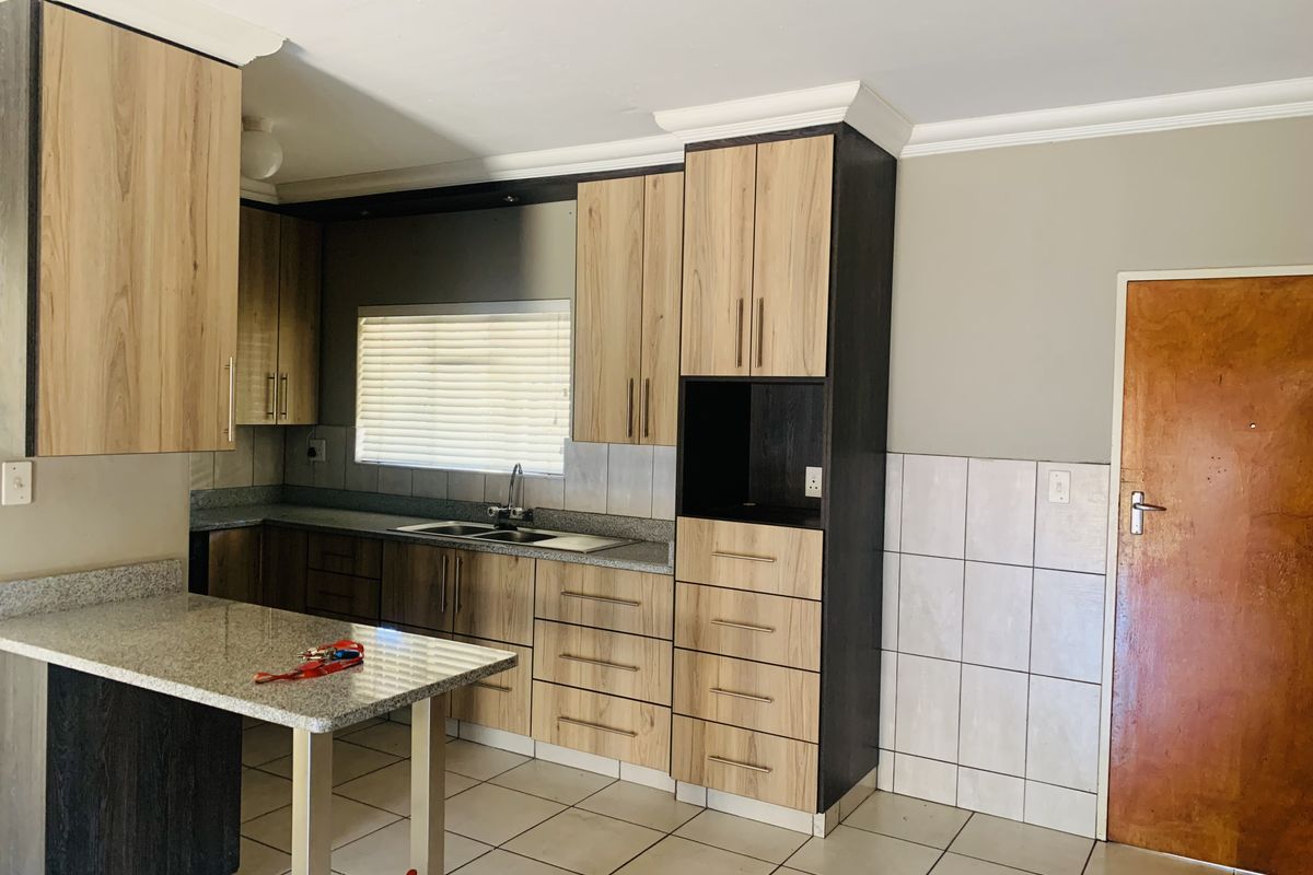 A functional kitchen featuring wood-look cabinetry, granite countertops, a double sink, and tiled flooring, offering a clean and practical workspace.