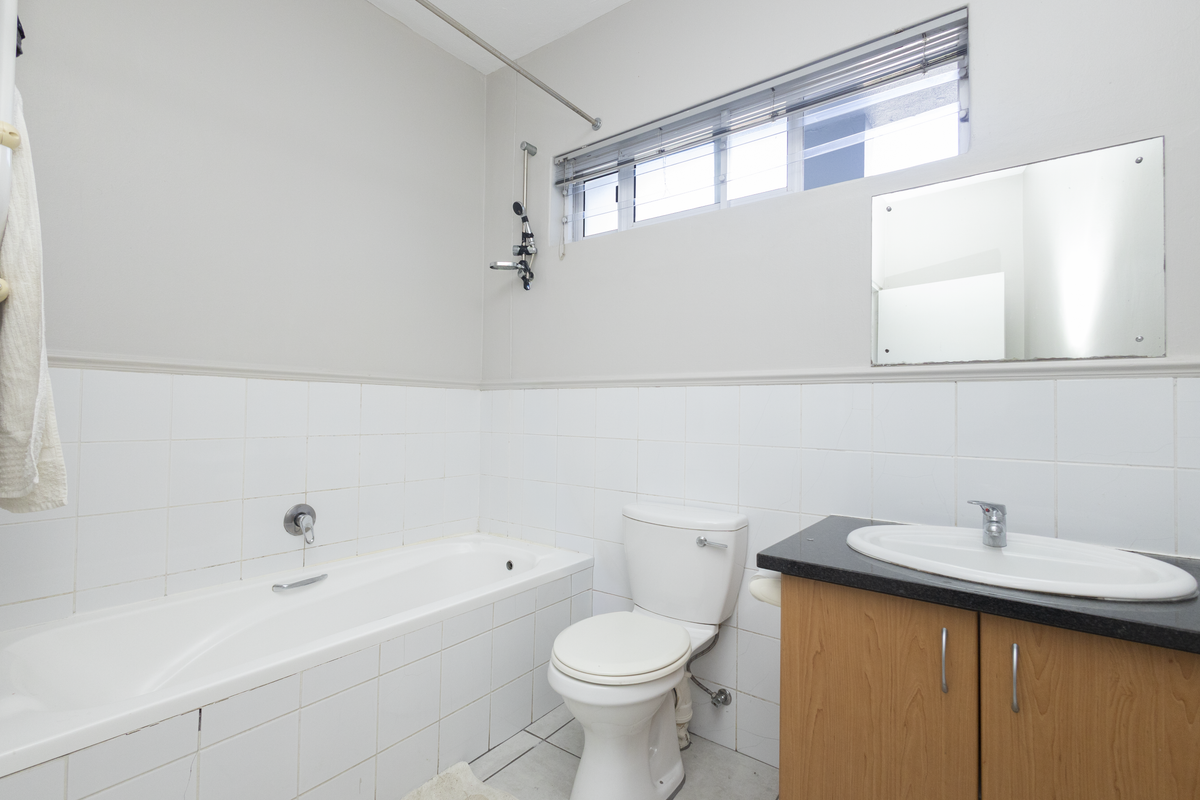A functional bathroom featuring a bathtub, toilet, and vanity cabinet with a basin, finished with white wall tiles and a wall-mounted mirror.