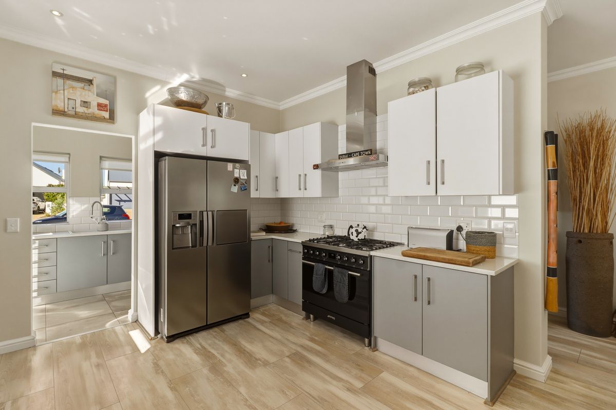 Modern kitchen featuring two-tone cabinetry, subway tile backsplash, stainless steel extractor fan, and a gas range, with an adjacent scullery area.