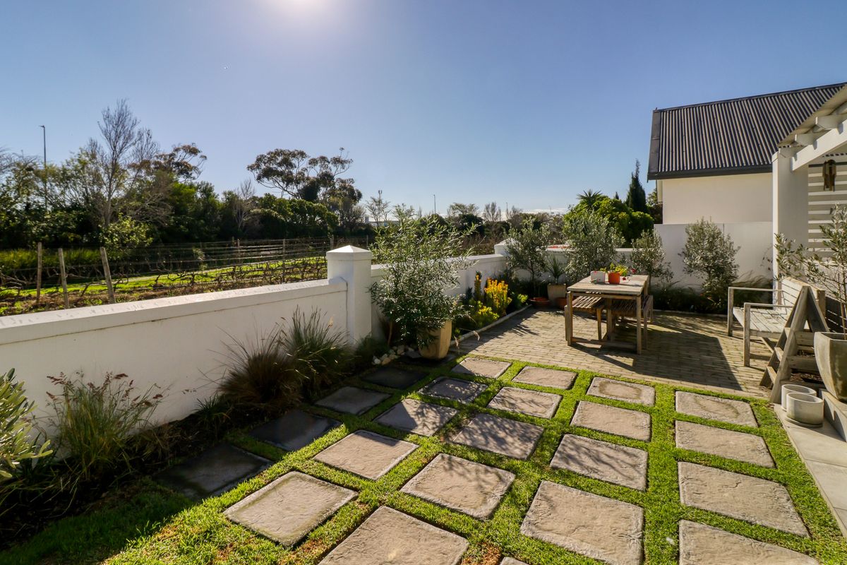 A well-maintained rear patio area featuring paved sections, a grass grid, and a perimeter wall overlooking a vineyard.
