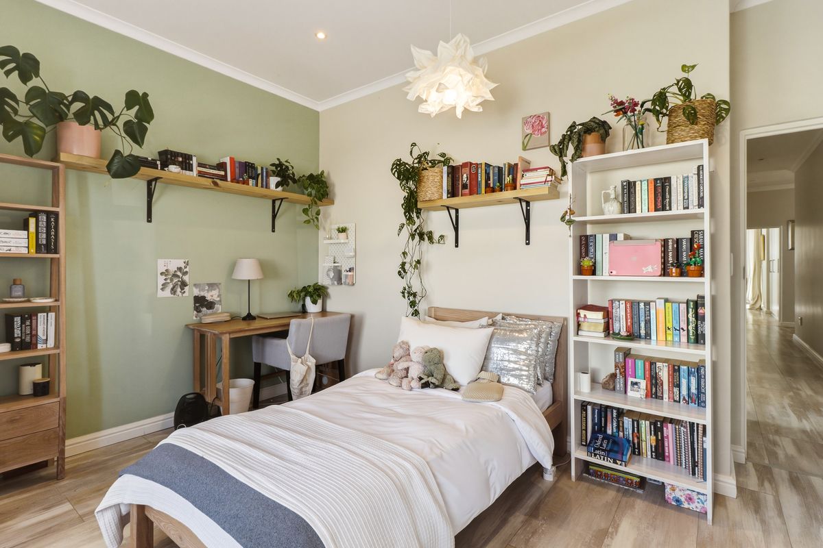A cozy bedroom featuring light wood-look flooring, a sage green accent wall, and built-in wooden shelving units.