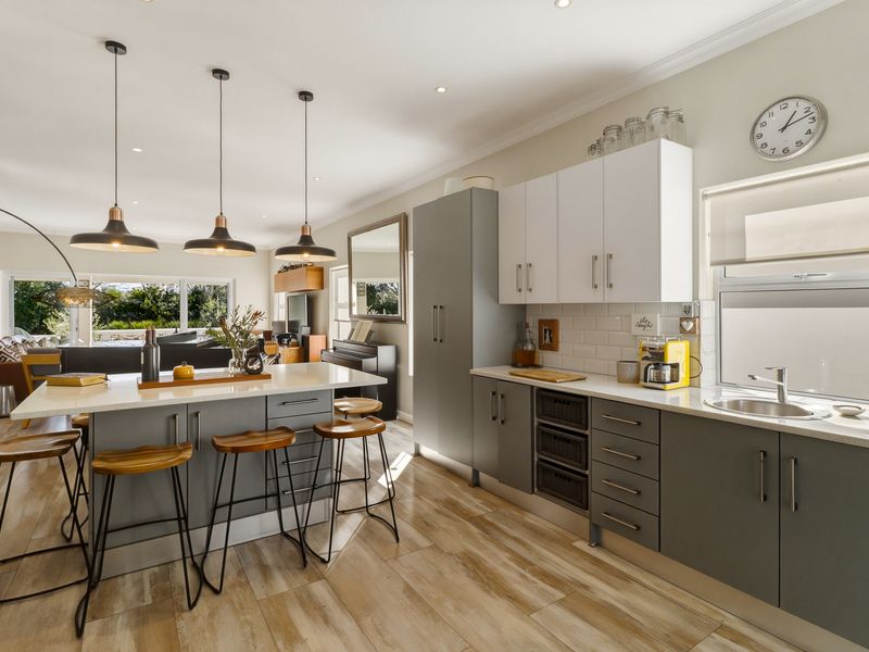 Modern open-plan kitchen featuring a central island with breakfast bar, sleek cabinetry, stone countertops, and integrated lighting, flowing into the adjacent living area.