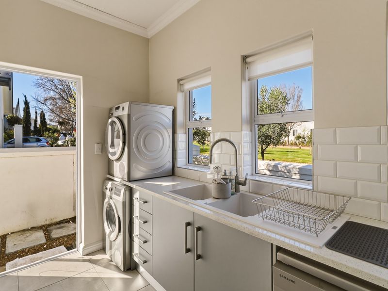 A functional laundry room featuring modern grey cabinetry, a stone countertop, a built-in sink, and space for stacked laundry appliances with direct outdoor access.