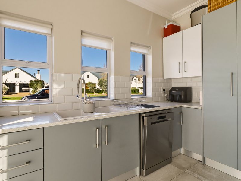 A bright and modern kitchen featuring light grey cabinetry, white subway tile backsplash, stone countertops, and a double basin sink with a gooseneck faucet.