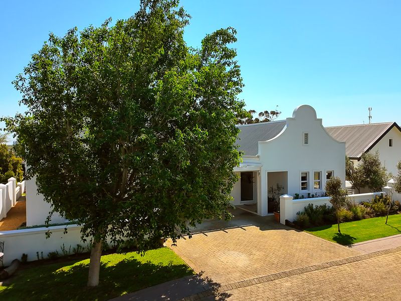 A well-maintained front elevation of a house featuring a gabled roof, paved driveway, and landscaped garden area.