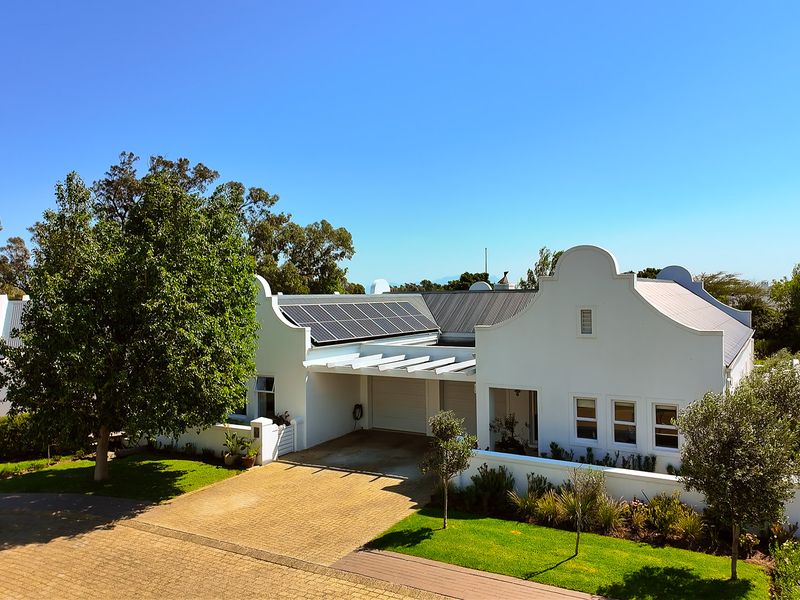 A well-maintained single-story home featuring a classic Cape Dutch-style gable, solar panels, a double garage, and a neatly landscaped front garden.