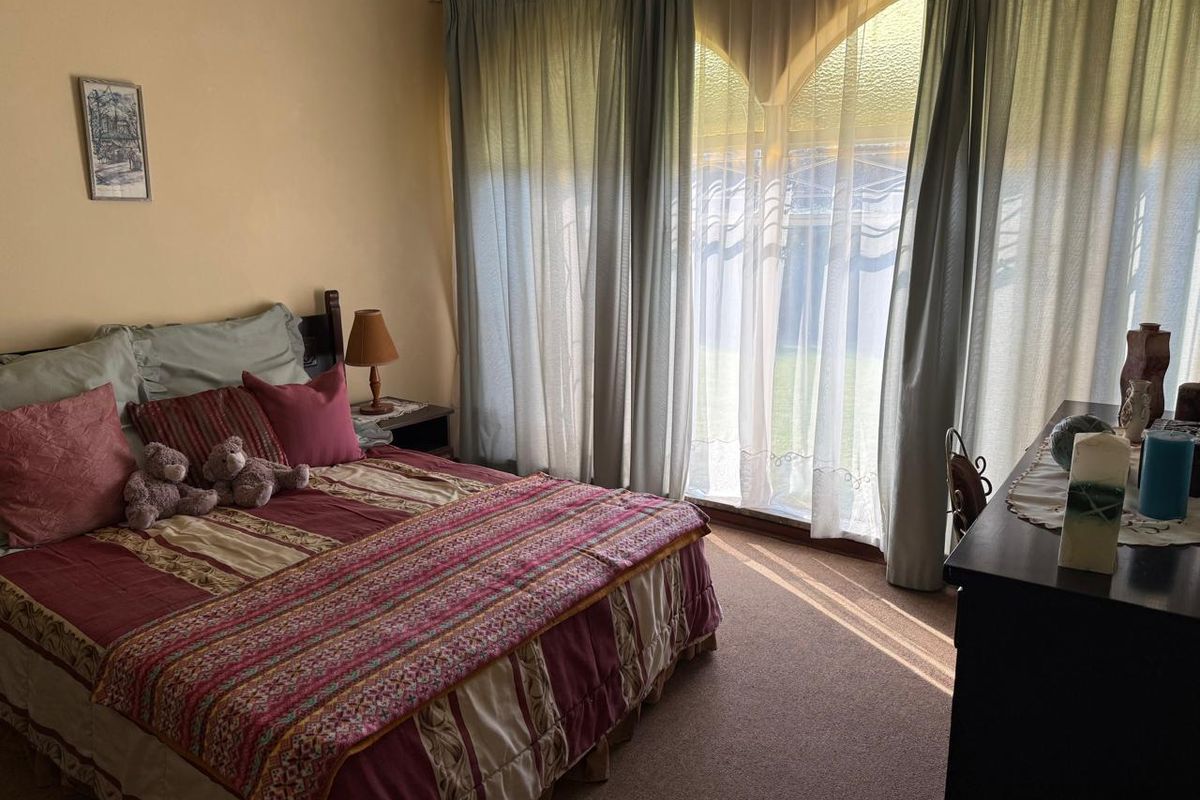 A bedroom featuring carpeted flooring and a large arched window with curtains, providing natural light and garden views.