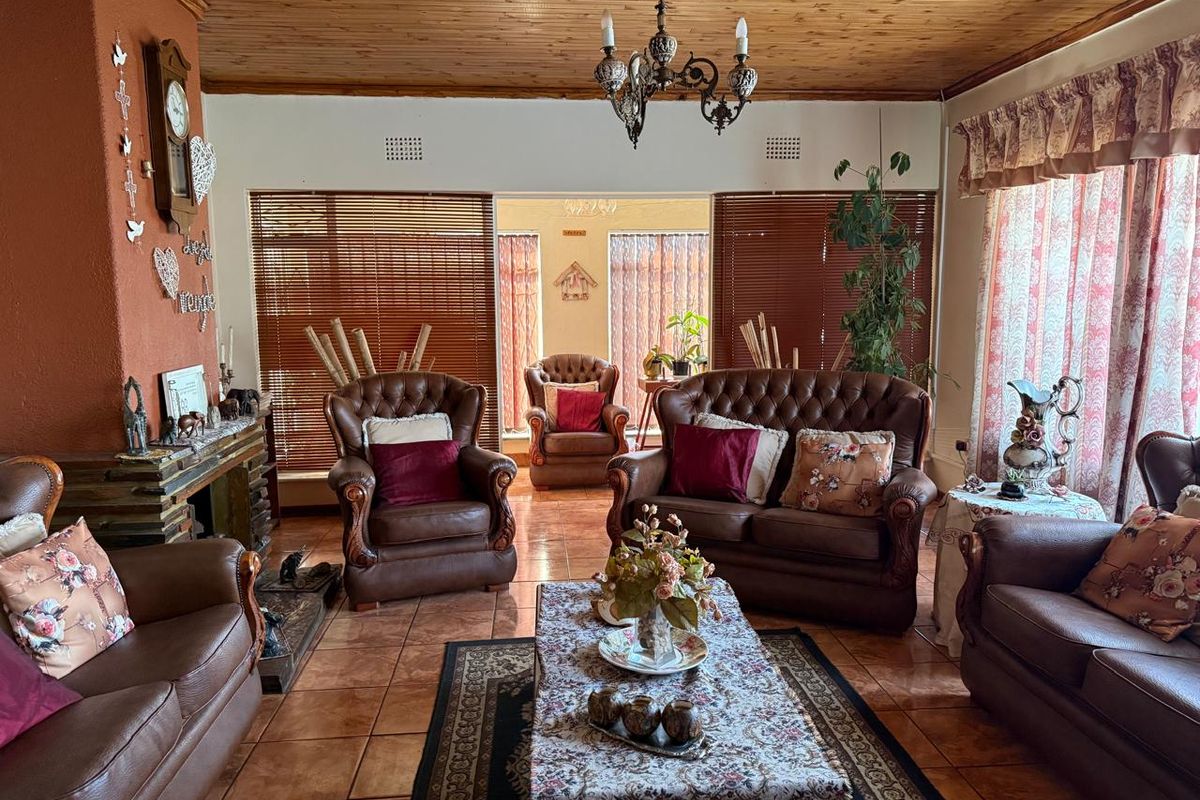 Spacious living room featuring a timber ceiling, tiled flooring, and a brick fireplace, offering a traditional and warm atmosphere.