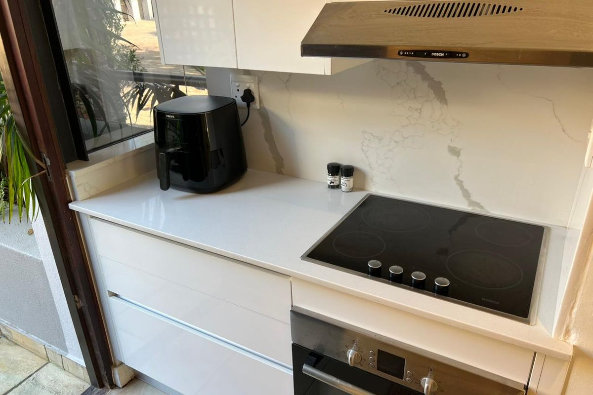 Modern kitchen featuring white gloss cabinetry, stone countertops, a built-in Bosch electric hob, and a stainless steel extractor fan.