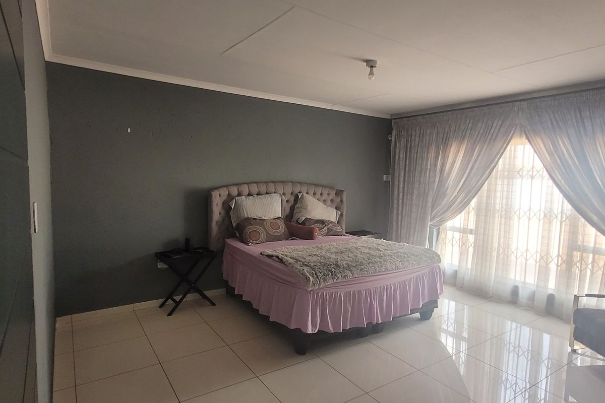 Spacious bedroom featuring large format floor tiles, dark accent wall, and expansive window with integrated security gate.