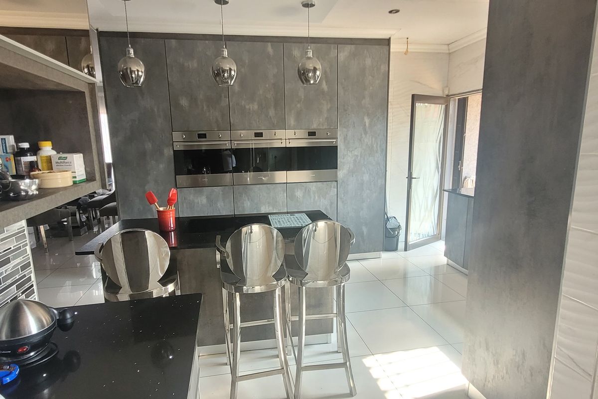 Modern kitchen featuring sleek grey cabinetry, integrated wall ovens, a central island with breakfast bar seating, and polished floor tiles.