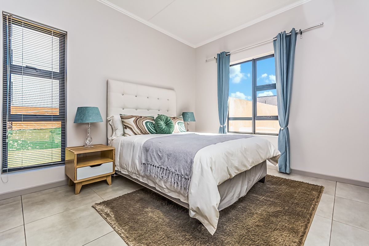 A bright and well-maintained bedroom featuring neutral tiled flooring, large windows with fitted blinds, and clean wall finishes.