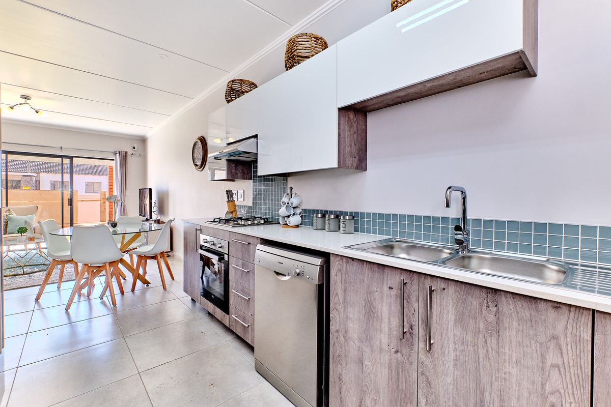 Modern open-plan kitchen featuring sleek cabinetry, gas hob, built-in oven, and tiled backsplash, flowing seamlessly into the dining and living area.