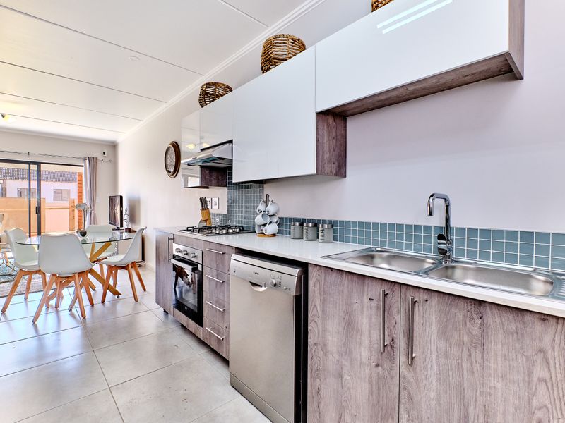 Modern open-plan kitchen featuring sleek cabinetry, gas hob, built-in oven, and tiled backsplash, flowing seamlessly into the dining and living area.