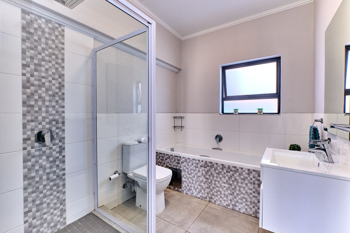 Modern bathroom featuring a glass-enclosed shower, a bathtub with mosaic tile detailing, a vanity basin, and a toilet with neutral wall finishes.