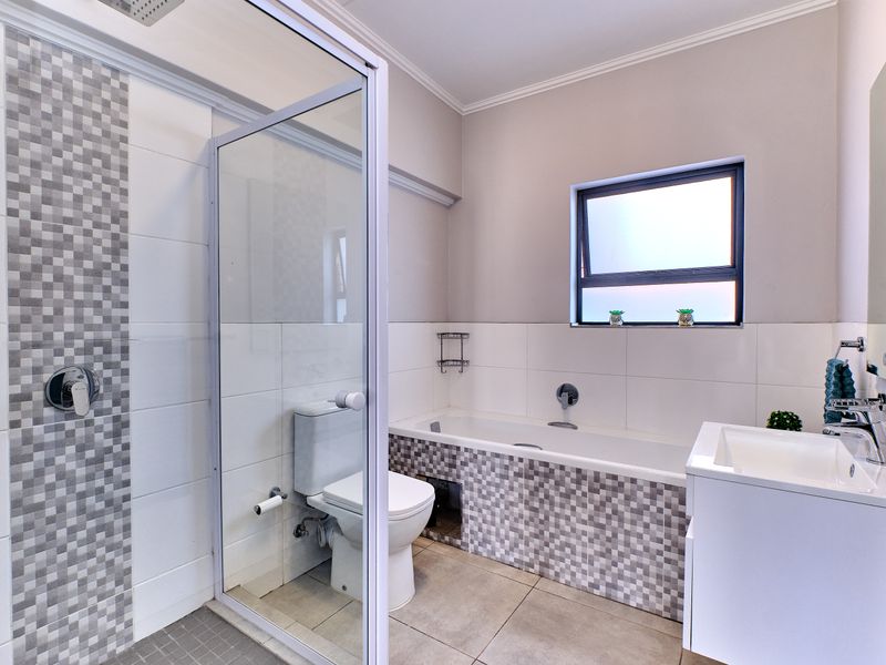 Modern bathroom featuring a glass-enclosed shower, a bathtub with mosaic tile detailing, a vanity basin, and a toilet with neutral wall finishes.