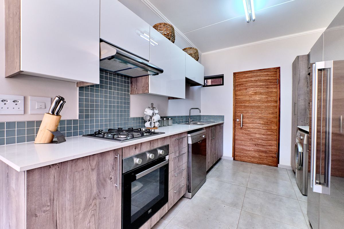 Modern kitchen featuring sleek white and wood-grain cabinetry, gas hob, built-in oven, extractor fan, and tiled backsplash with neutral floor tiles.
