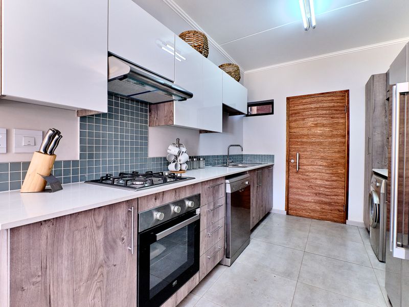 Modern kitchen featuring sleek white and wood-grain cabinetry, gas hob, built-in oven, extractor fan, and tiled backsplash with neutral floor tiles.