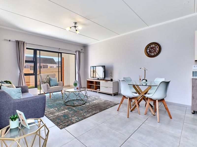 A bright open-plan living and dining area featuring neutral tiled flooring, modern finishes, and a sliding glass door leading to an outdoor space.