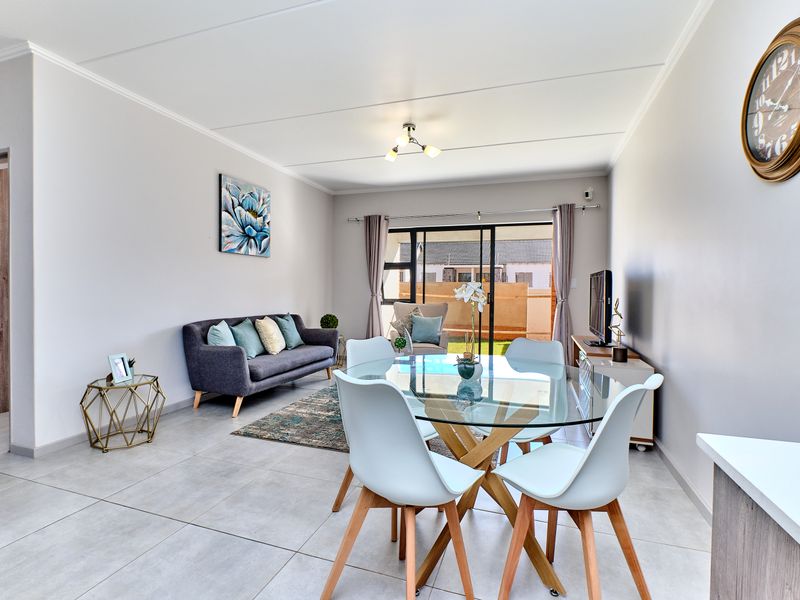 An open-plan living and dining area featuring neutral tiled flooring, modern lighting, and a sliding glass door providing access to the outdoor space.