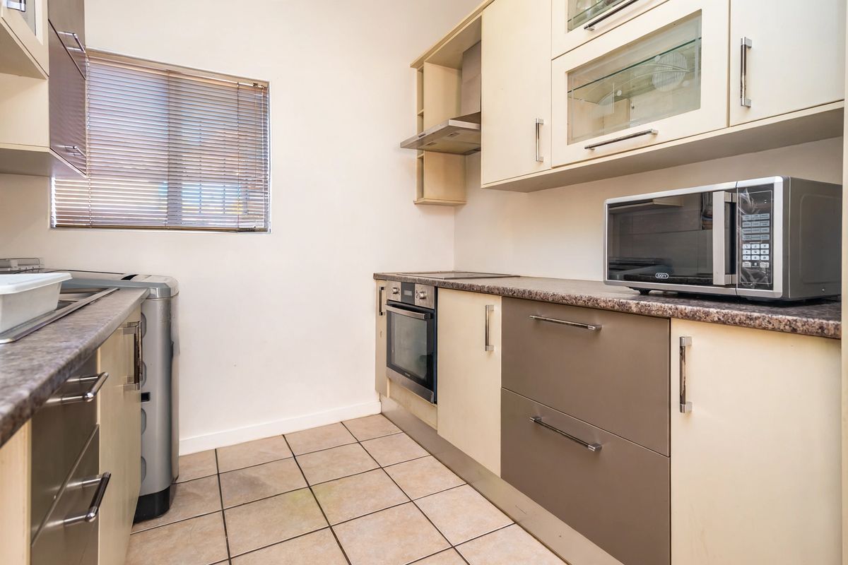 A functional kitchen featuring built-in cabinetry, laminate countertops, a built-in oven, extractor fan, and ceramic floor tiles.