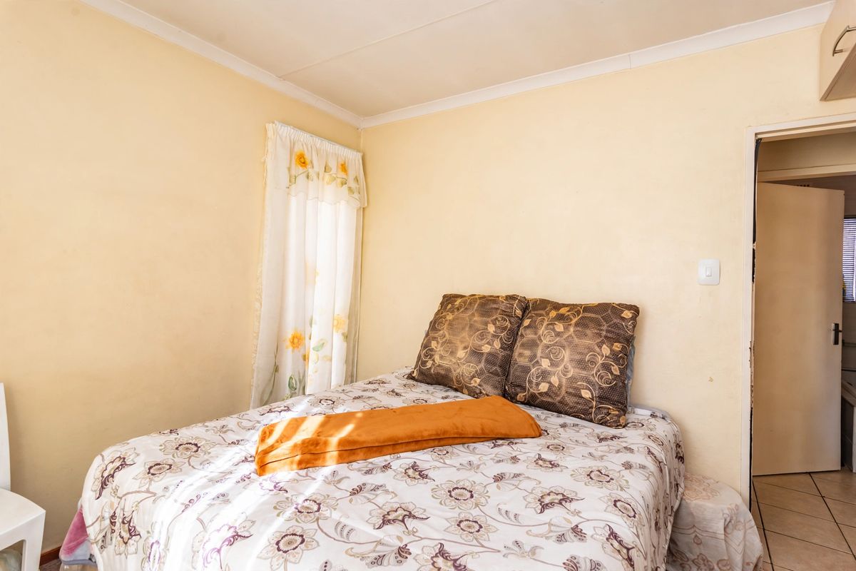 A compact bedroom featuring tiled flooring and neutral wall finishes, providing a functional space with direct access to an adjacent room.