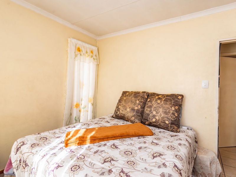 A compact bedroom featuring tiled flooring and neutral wall finishes, providing a functional space with direct access to an adjacent room.