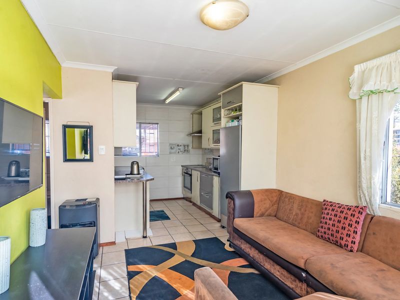 Open-plan living area featuring a compact kitchen with built-in cabinetry, tiled flooring, and a breakfast counter, seamlessly connected to the lounge space.
